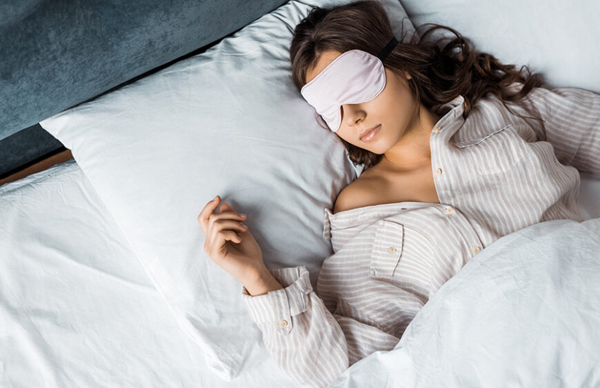 young brunette woman sleeping in eye mask in bed