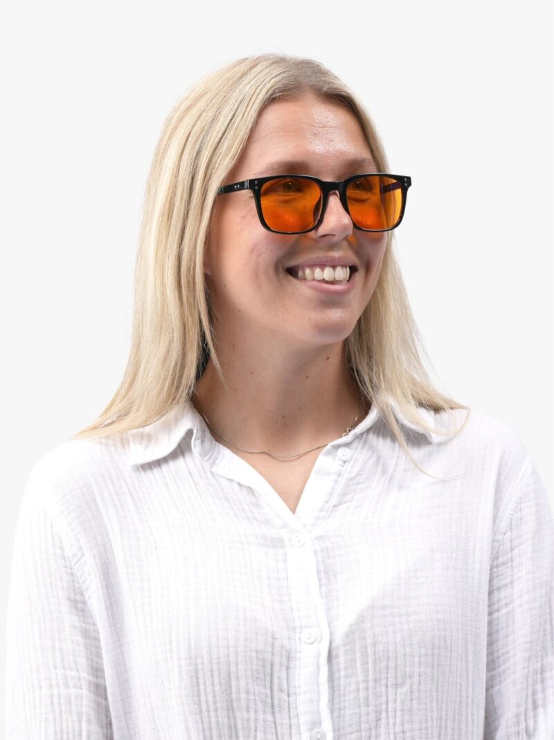 Smilende kvinde i hvid skjorte iført Obsidian 90 sorte solbriller med orange linser