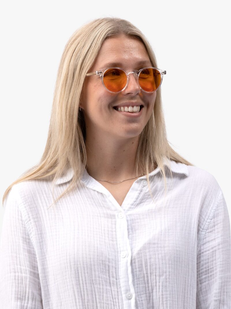 Smilende kvinde med langt blondt hår i gennemsigtige stelbriller med orange linser og hvid skjortebluse