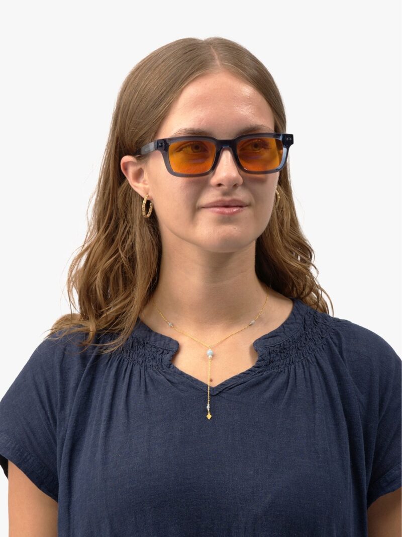 Kvinde iført Eclipse 90 blå rektangulære solbriller med orange linser, guldøreringe og blå bluse