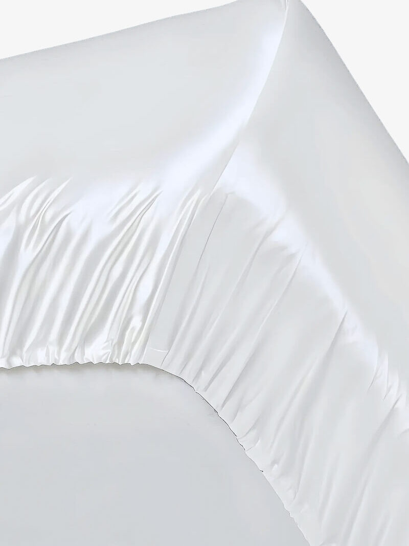 Hjørne af hvidt satinlagen med elastisk kant og glansfulde rynker