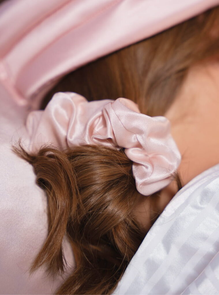 Nærbillede af brunt hår samlet med lyserød satin scrunchie på silkepude