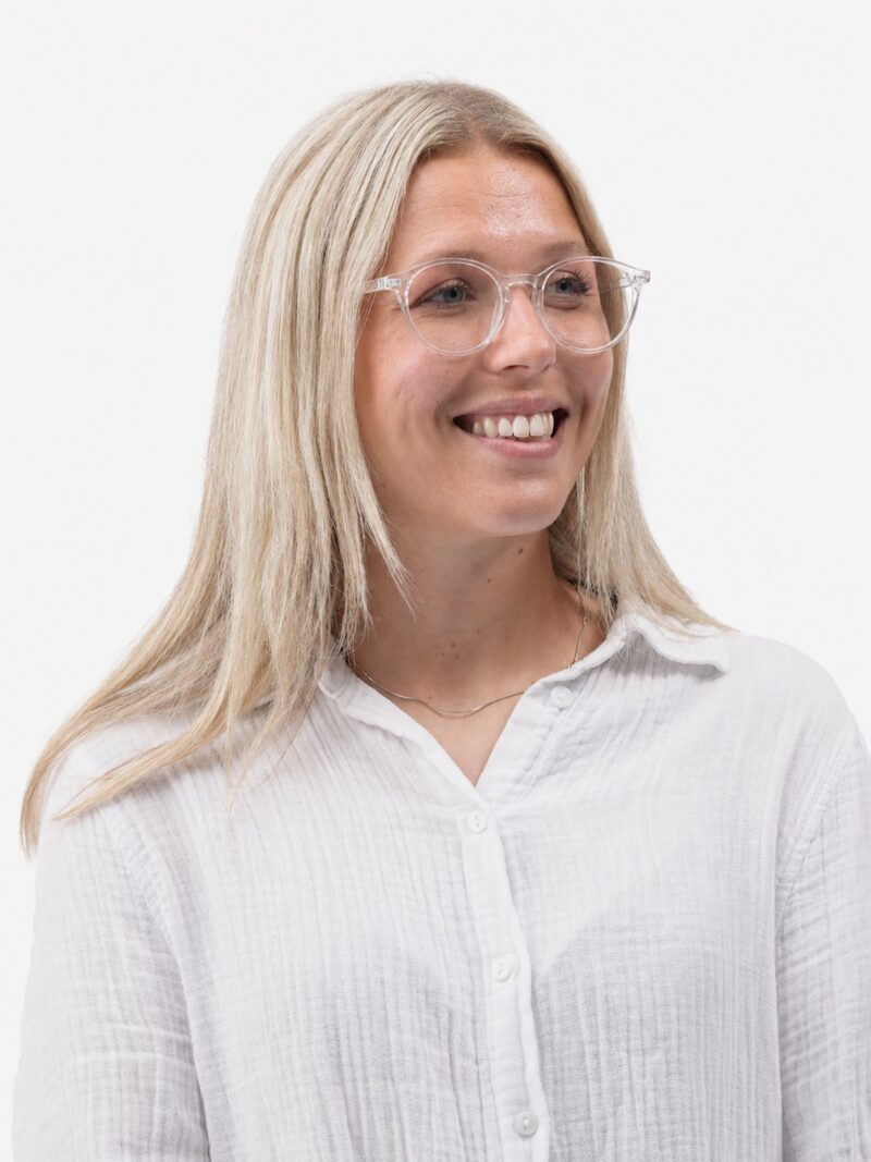 Smilende ung kvinde med blondt hår, klare runde briller og hvid skjorte, kigger til højre