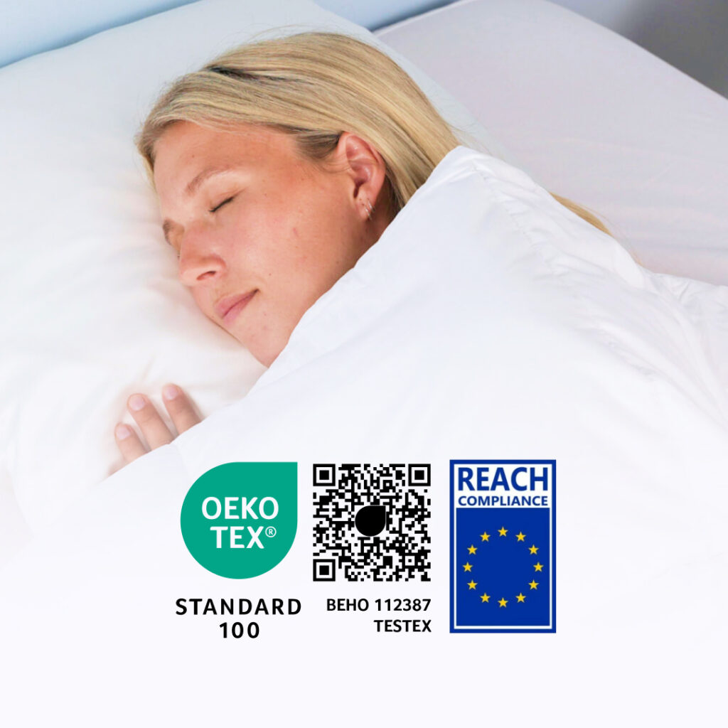 Sovende person under hvid dyne med OEKO-TEX Standard 100, REACH certificeringslogoer og QR-kode