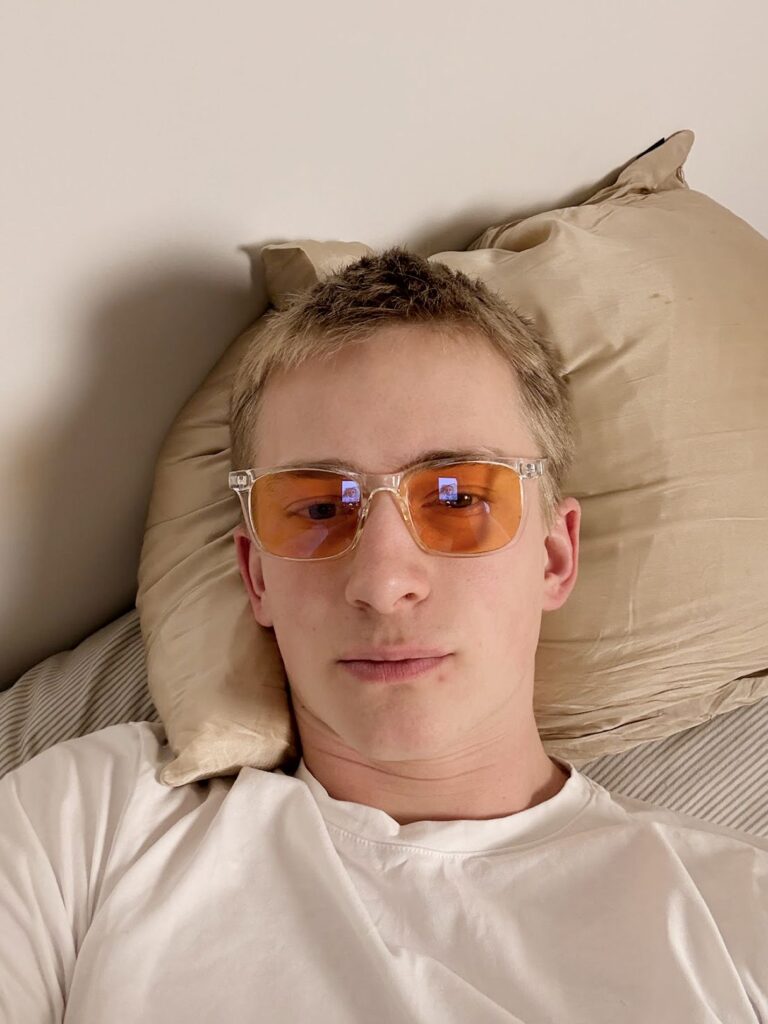 Ung person liggende på pude med orangetonede blålysbriller og hvid t-shirt